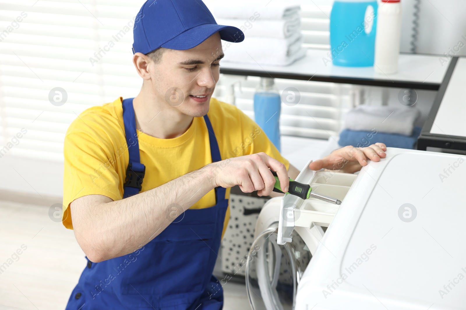 Photo of Smiling plumber with screwdriver repairing washing machine in bathroom