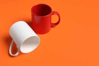 Photo of Red and white ceramic mugs on orange background, space for text