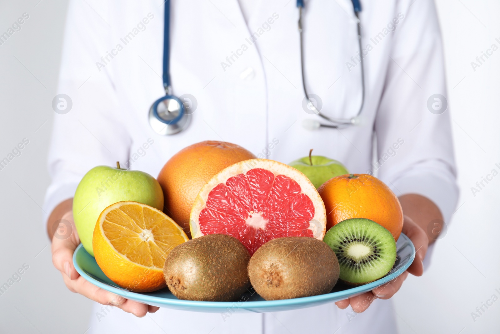 Photo of Female nutritionist with fruits on light background, closeup