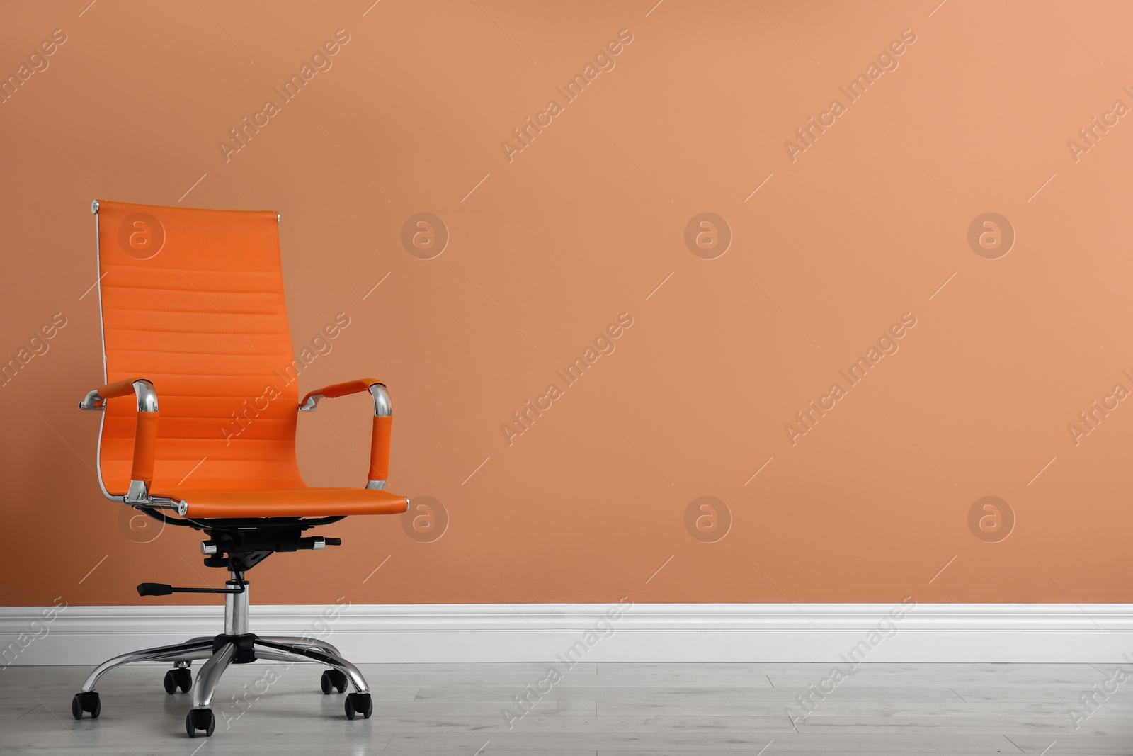 Photo of Modern office chair near orange coral wall indoors. Space for text