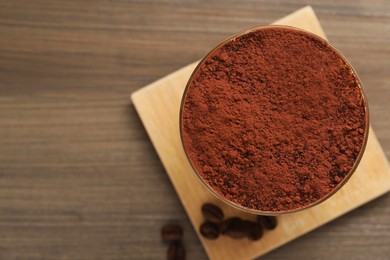 Delicious tiramisu in glass and coffee beans on wooden table, top view. Space for text