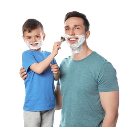 Photo of Little son applying shaving foam onto dad's face against white background