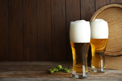 Photo of Composition with tasty beer and fresh green hops on wooden table. Space for text