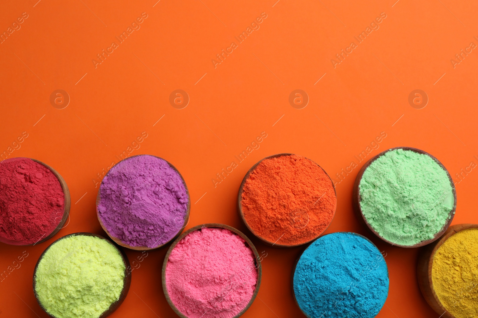 Photo of Colorful powders in bowls on orange background, flat lay with space for text. Holi festival celebration