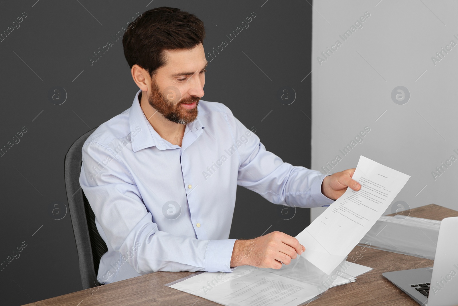 Photo of Businessman putting document into punched pocket at wooden table in office