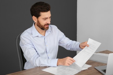 Businessman putting document into punched pocket at wooden table in office