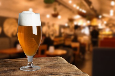 Image of Glass with fresh beer on wooden table in pub, space for text