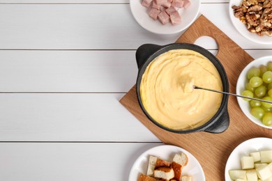 Photo of Fondue pot with tasty melted cheese, fork and different snacks on white wooden table, flat lay. Space for text
