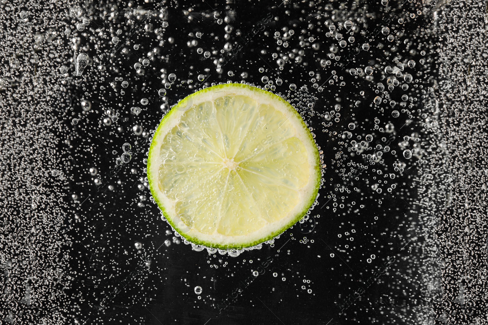 Photo of Juicy lime slice in soda water against black background, closeup