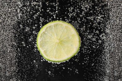 Photo of Juicy lime slice in soda water against black background, closeup