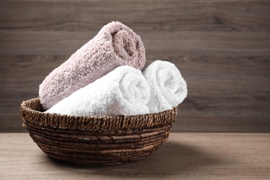 Photo of Rolled soft towels in wicker basket on wooden table. Space for text