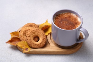 Photo of Cup of hot drink, cookies and autumn leaves on light grey textured table, closeup