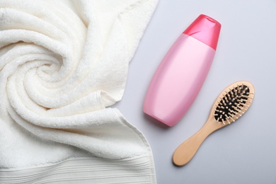 Bottle with shampoo, towel and brush on color background, flat lay