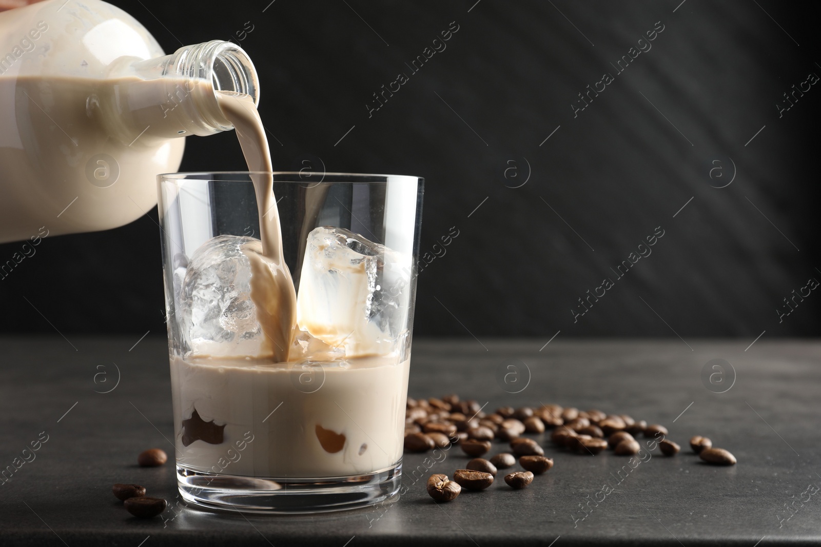 Photo of Pouring coffee cream liqueur into glass at grey table, closeup. Space for text