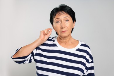 Senior woman cleaning ear with cotton swab on light grey background