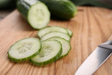 Photo of Cut cucumber and knife on wooden board, closeup