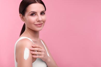 Beautiful woman with smear of body cream on her shoulder against pink background. Space for text
