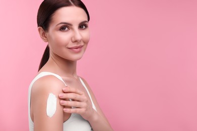 Photo of Beautiful woman with smear of body cream on her shoulder against pink background. Space for text