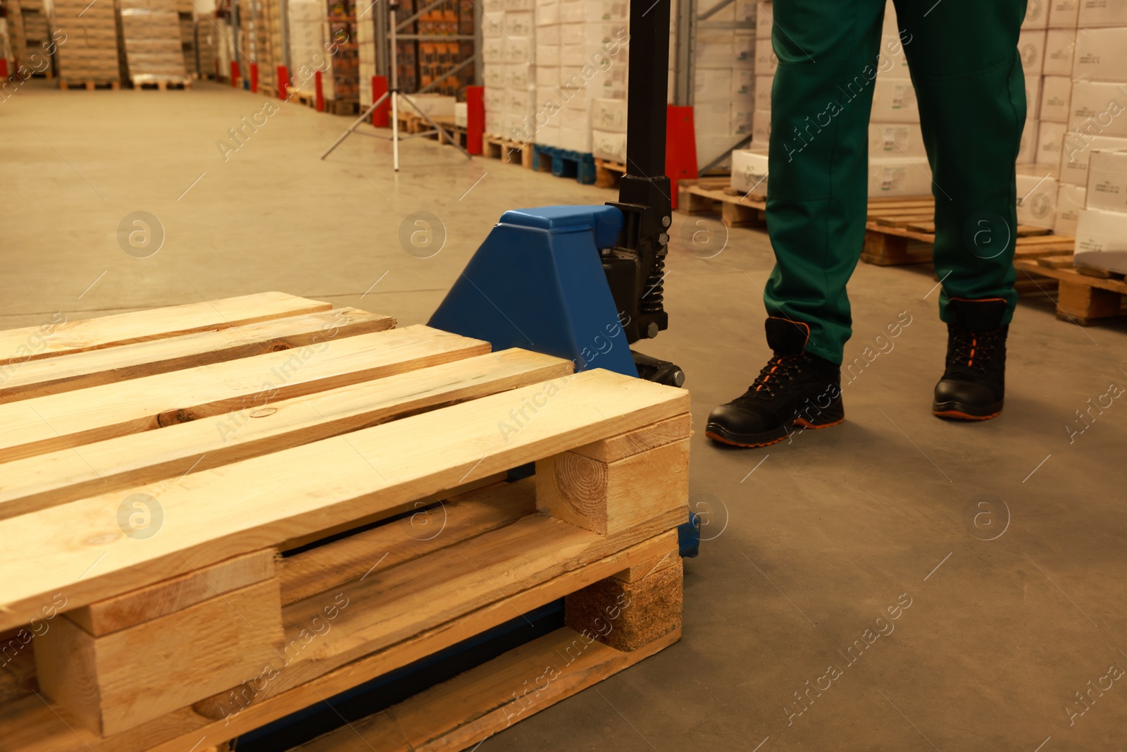 Image of Worker moving wooden pallets with manual forklift in warehouse, closeup