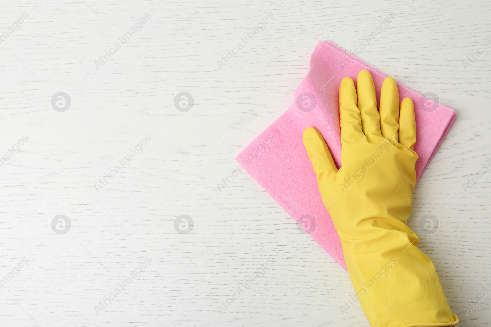 Photo of Person in gloves wiping white wooden table with rag, top view. Space for text