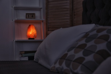 Photo of Himalayan salt lamp on shelf in dark bedroom