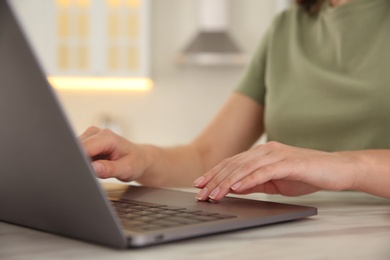 Photo of Woman working with modern laptop at marble table, closeup