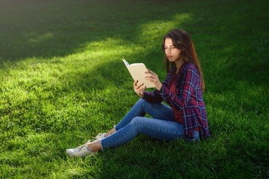 Photo of Young woman reading book on green grass outdoors