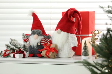 Photo of Funny Christmas gnomes and gift boxes on commode in room with festive decoration