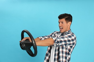 Emotional man with steering wheel on light blue background