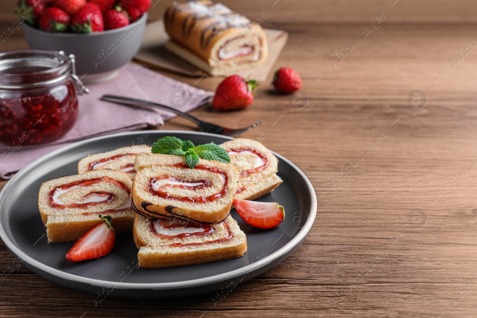 Photo of Tasty cake roll with strawberry jam and cream on wooden table, space for text