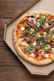 Photo of Tasty pizza with anchovies, arugula and olives on wooden table, top view