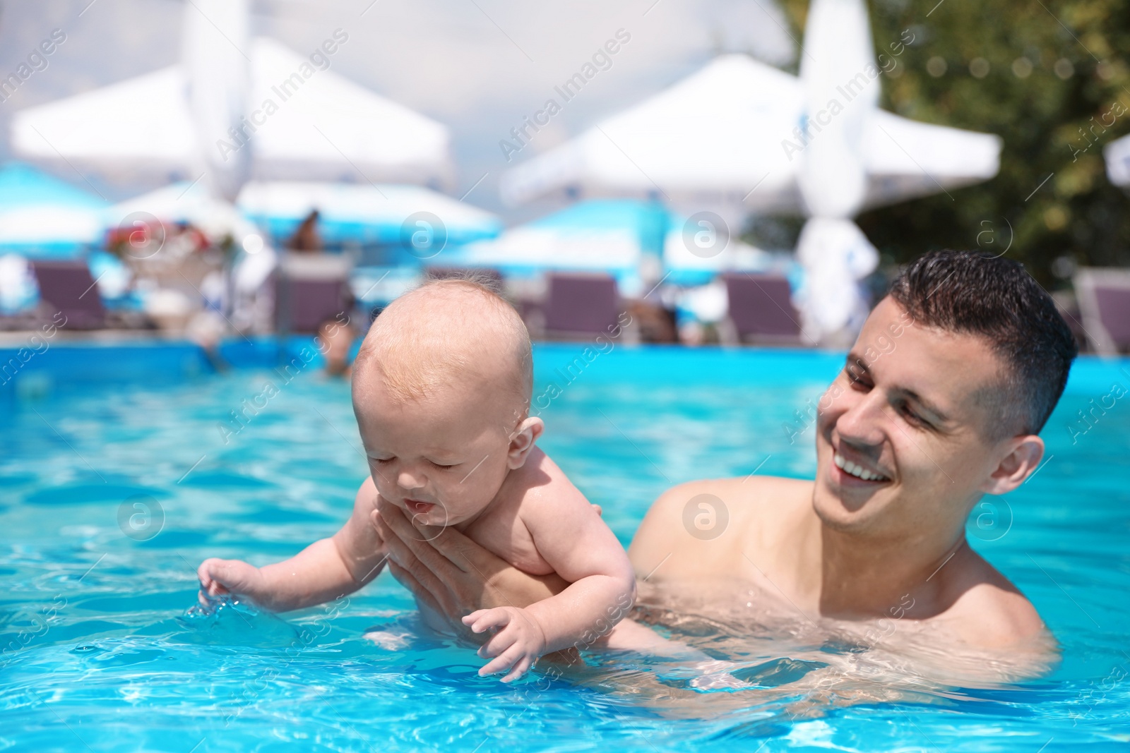 Photo of Man with his little baby in swimming pool on sunny day, outdoors