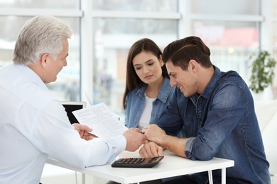 Photo of Young couple discussing pension plan with mature consultant in office