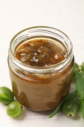 Photo of Jar of delicious gooseberry jam and fresh berries on white wooden table, closeup