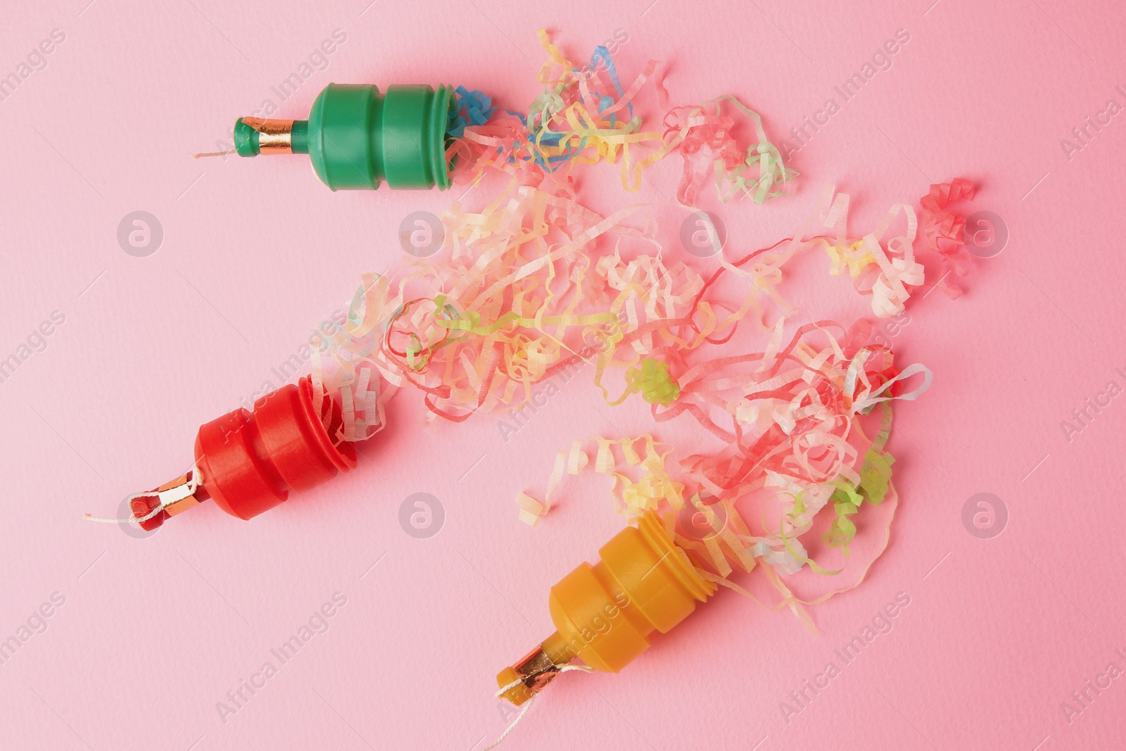 Photo of Beautiful serpentine bursting out of small party poppers on pink background, flat lay