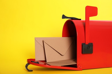 Open red letter box with envelopes on yellow background, closeup