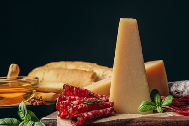 Photo of Delicious parmesan cheese, sausage slices, honey, bread and basil on wooden board, closeup