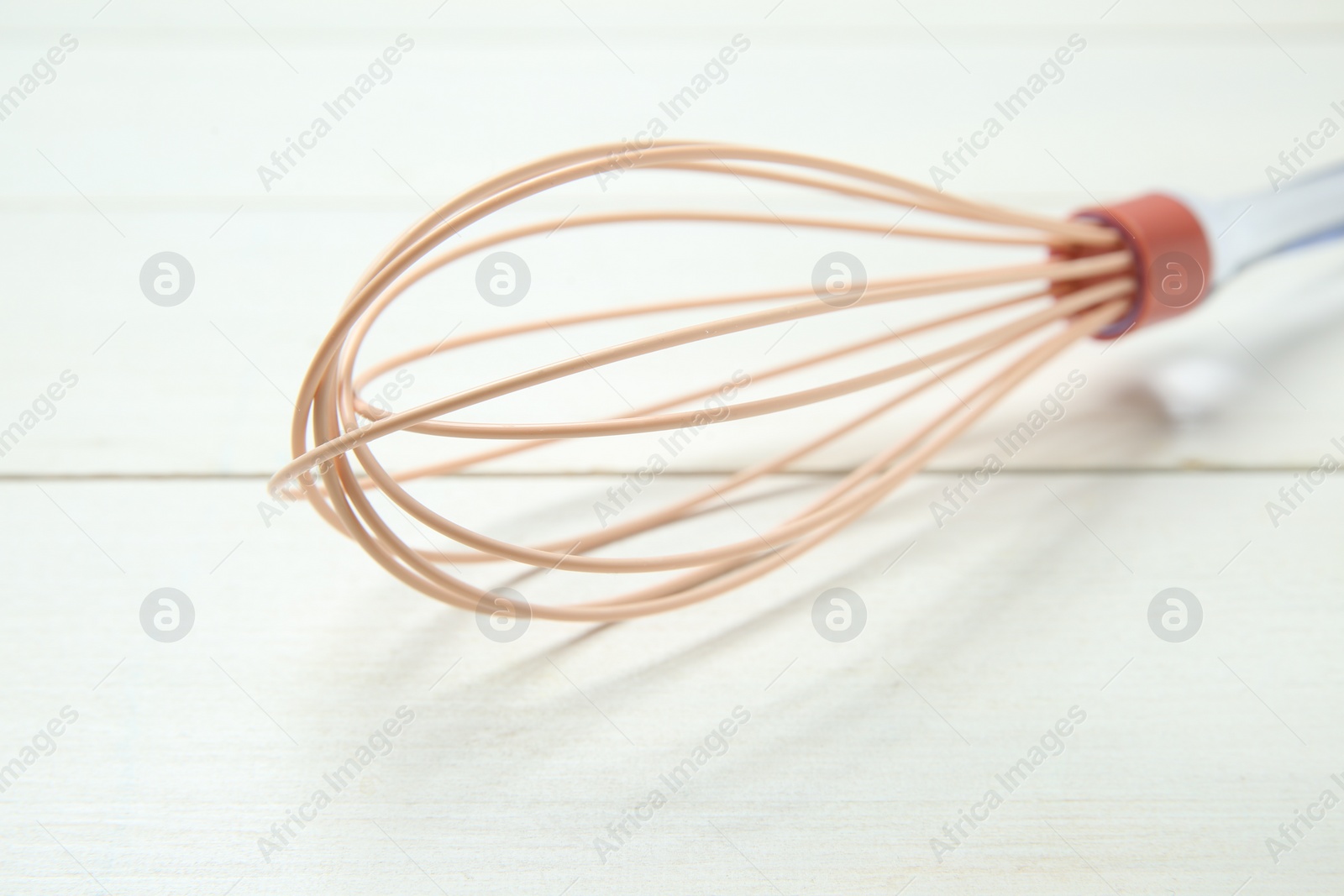 Photo of One whisk on white wooden table, closeup