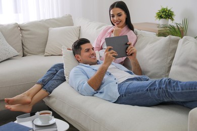 Photo of Couple with tablet resting on sofa in living room