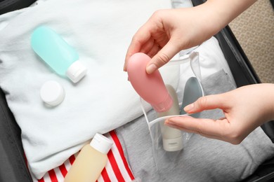 Photo of Woman putting small bottle with personal care product into plastic bag, closeup. Cosmetic travel kit