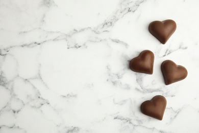 Tasty heart shaped chocolate candies on white marble table, flat lay with space for text. Happy Valentine's day