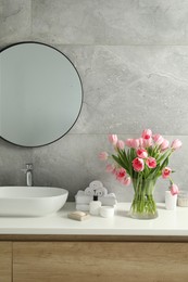 Photo of Vase with beautiful pink tulips and toiletries near sink in bathroom