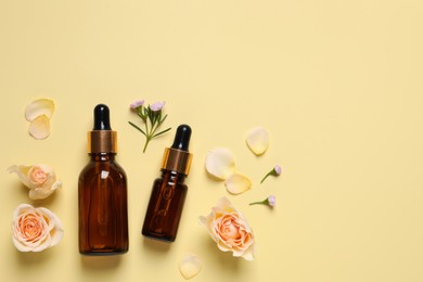 Photo of Bottles of cosmetic serum, beautiful flowers and petals on pale yellow background, flat lay. Space for text