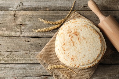 Tasty homemade tortillas, rolling pin and spikes on wooden table, top view. Space for text