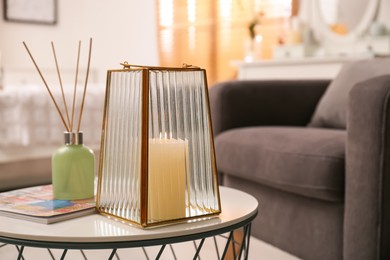 Photo of Stylish holder with burning candle and reed air freshener on table in room