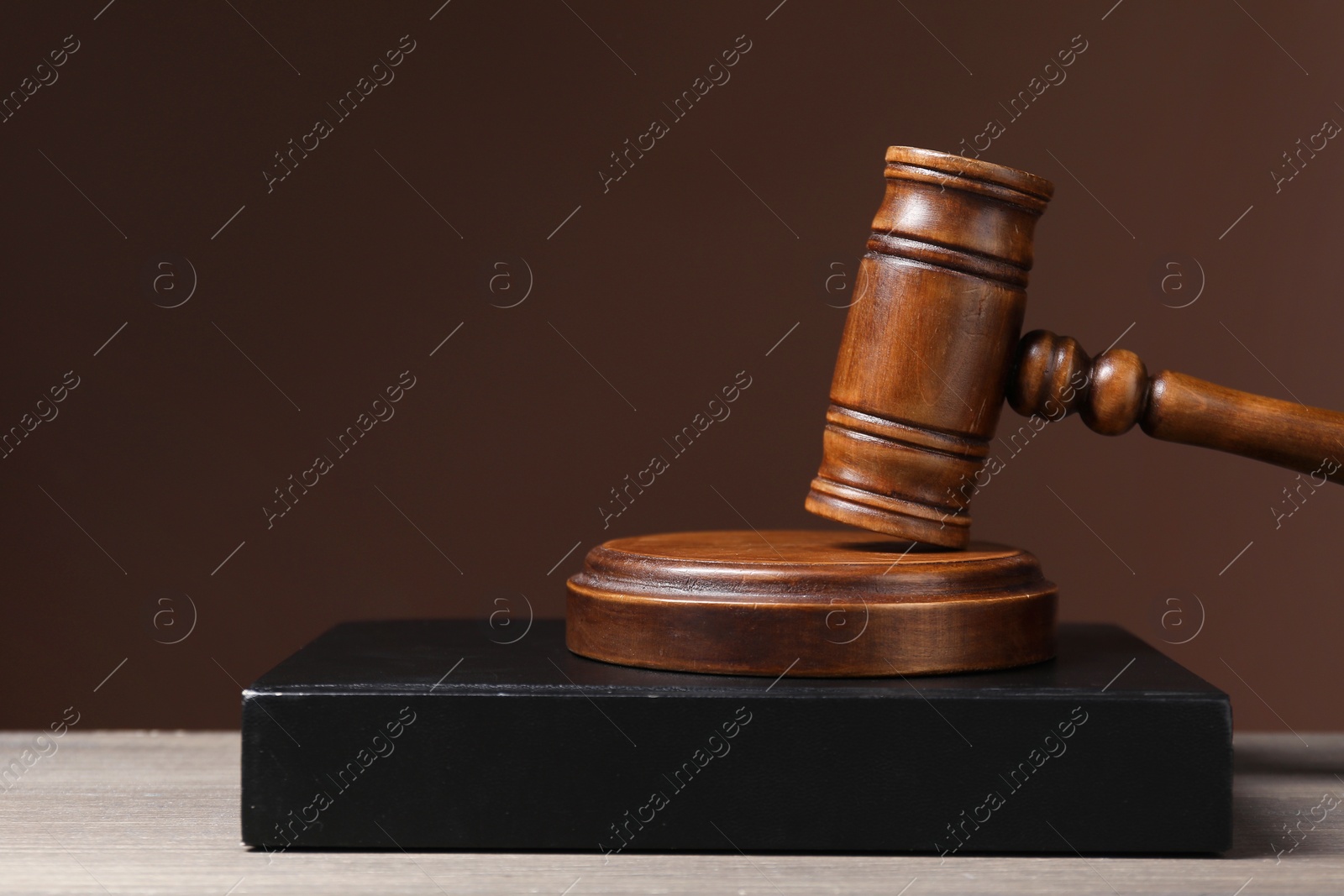 Photo of Law. Book and gavel on wooden table against brown background, space for text