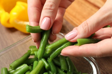 Photo of Woman putting green beans into glass container at table, closeup. Food storage