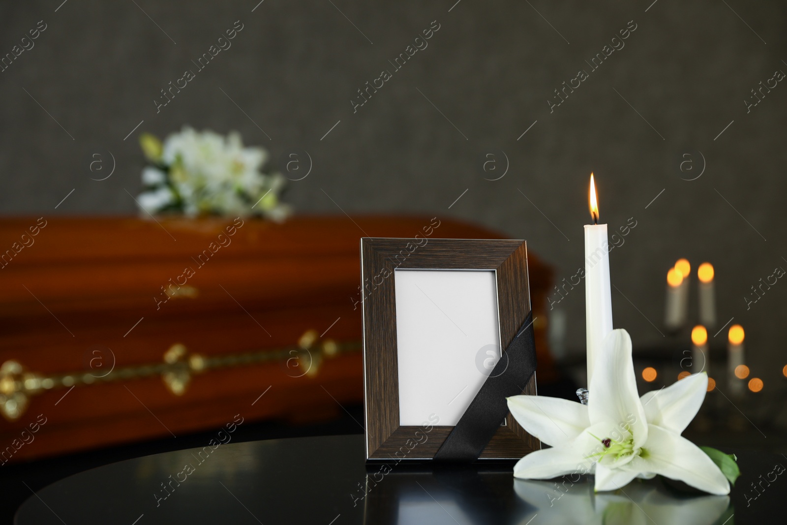 Photo of Black photo frame with burning candle and white lily on table in funeral home