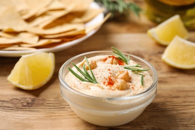 Photo of Delicious homemade hummus in glass bowl on wooden table