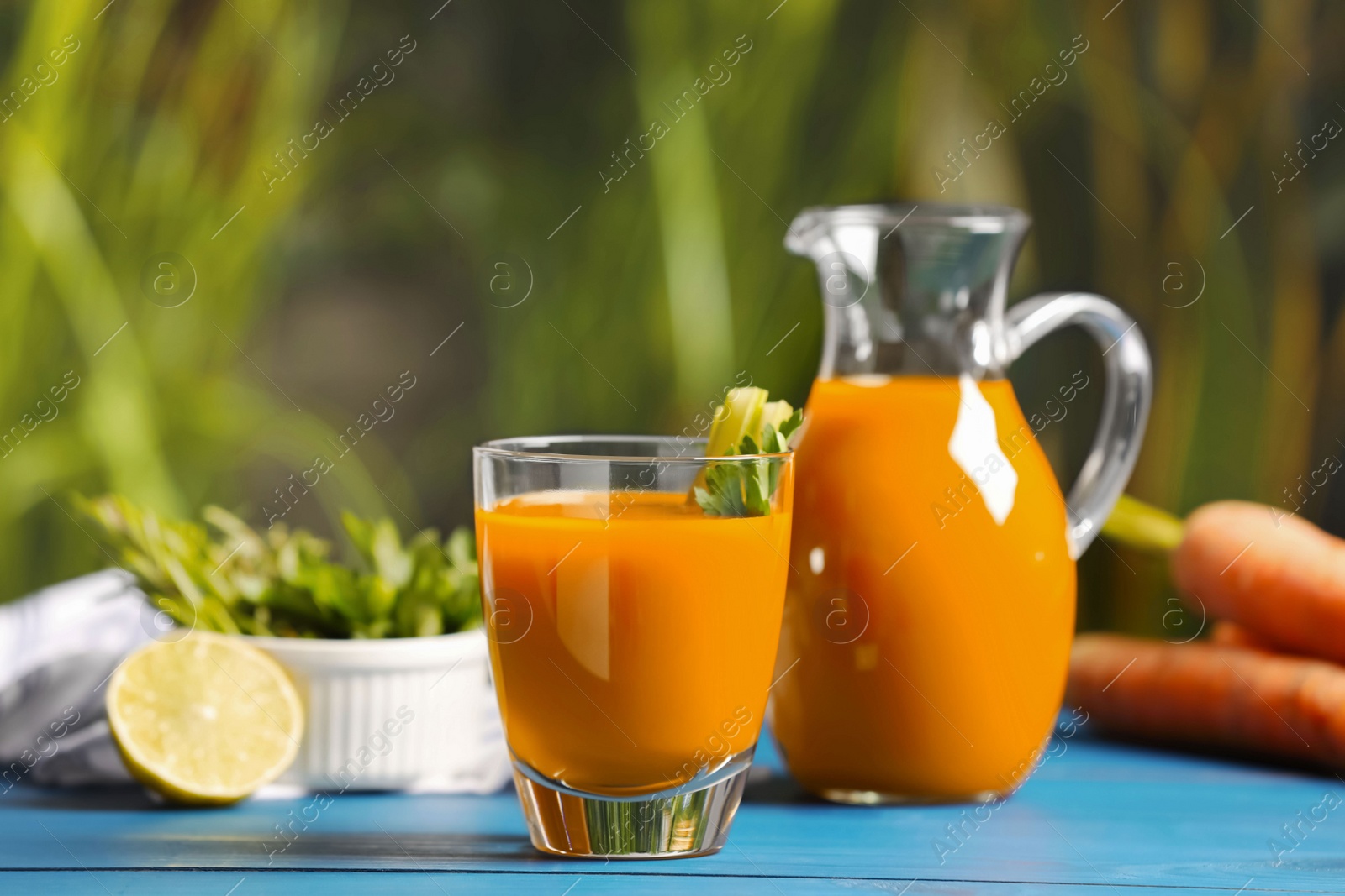 Photo of Tasty carrot juice on blue wooden table outdoors